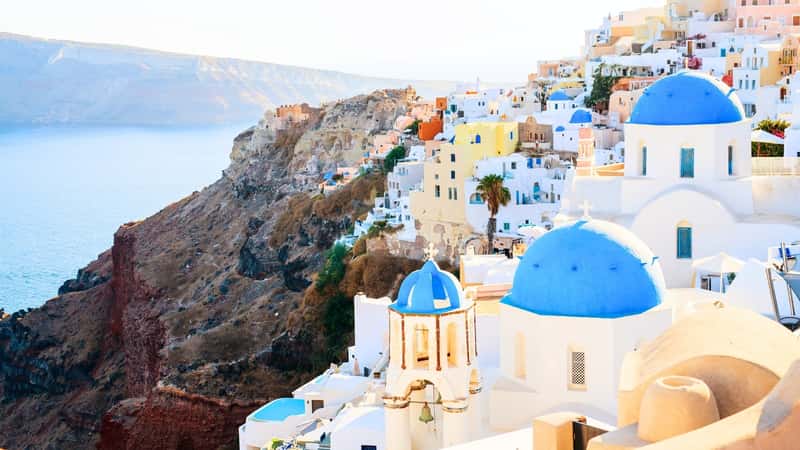 A blue-domed church in Oia overlooks the spectacular caldera surrounding Santorini Island in Greece. The church's architecture features traditional Cycladic style with whitewashed walls and striking blue domes. Surrounding the church is the breathtaking view of the caldera, characterized by rugged cliffs and deep blue waters.