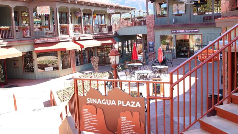 A photograph depicting a string of novelty gift shops and boutiques in uptown Sedona. Visitors can be seen walking along the sidewalk, suggesting pedestrian activity in the area.