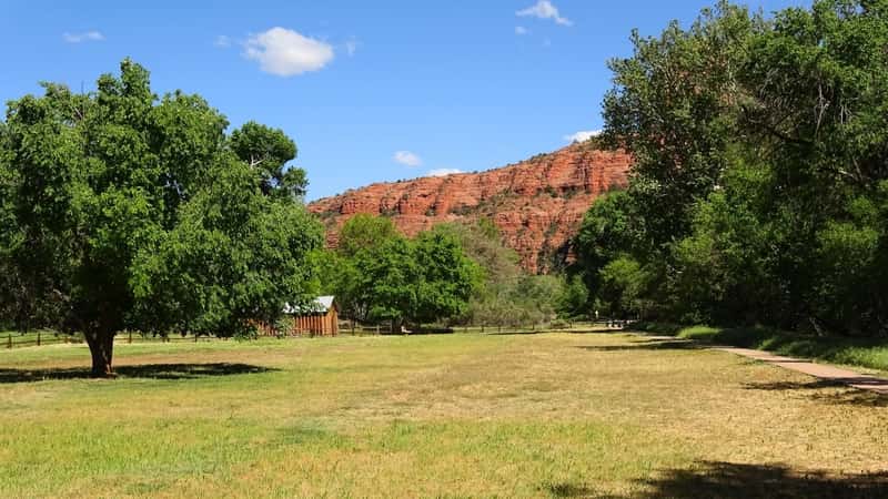 A photograph depicting a serene scene of a manicured lawn adorned with trees. In the distance, a small building is visible against the backdrop of the majestic mountains of Sedona, Arizona. 