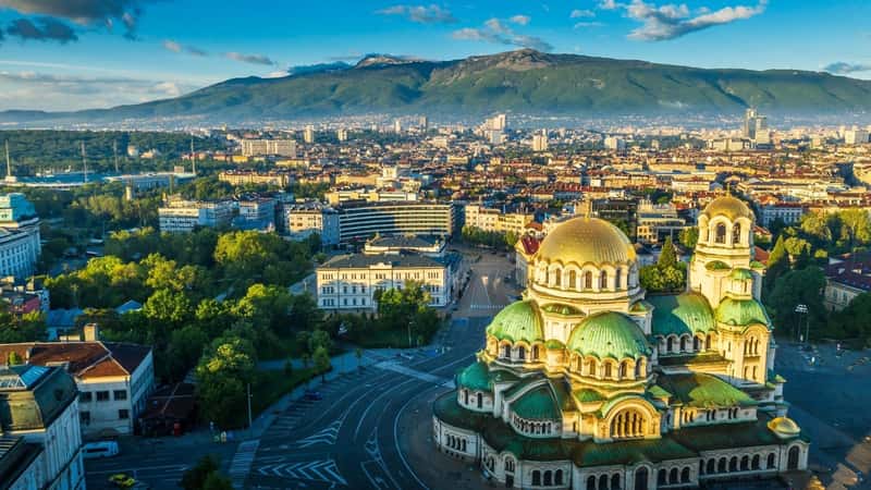 An aerial view captured by drone showcasing the Alexander Nevsky Russian Orthodox Cathedral in Sofia, Bulgaria. The image provides a comprehensive perspective of the cathedral's architectural features, including its distinctive domes and intricate details.