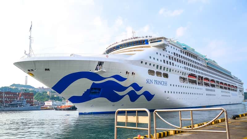 The image depicts the Sun Princess cruise ship, characterized by its white exterior with blue waves on the front of the ship and the "Sun Princess" inscription prominently displayed.