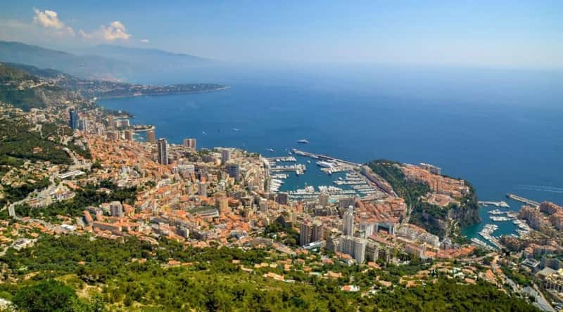 Tete de Chien in Monaco. The image features the iconic rocky promontory rising majestically against the Mediterranean Sea. The rugged cliffs and panoramic views of the French Riviera provide a breathtaking backdrop. At the foot of Tete de Chien, the coastal landscape unfolds, revealing the charming architecture of Monaco. Classic rooftops and facades, painted in warm hues, stand in contrast to the verdant greenery that surrounds the rocky outcrop.