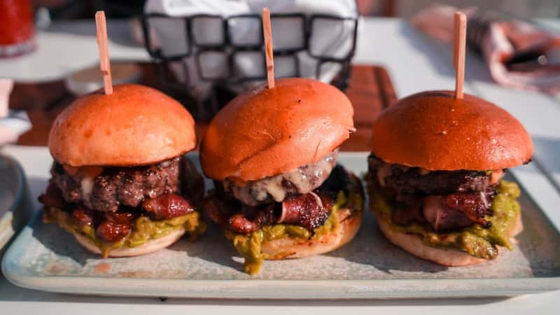 The image features a close-up view of three mini-burgers neatly arranged on a plate, each skewered for presentation.