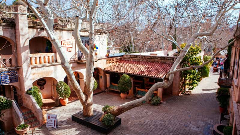 A photograph showcasing the iconic Tlaquepaque Arts & Crafts Village in Sedona, Arizona. The image highlights the village's stunning architecture, characterized by Spanish-inspired design elements such as arched doorways, red-tiled roofs, and intricate details. 