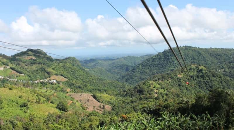 A photograph capturing the landscape surrounding Toro Verde Adventure Park in Puerto Rico. The image features elements of the park's infrastructure, including zipline installations and natural surroundings. The park's location within the lush Puerto Rican terrain is evident, with verdant foliage and hilly landscapes framing the scene.