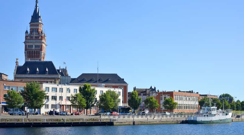 A side view capturing the Town Hall of Dunkirk, featuring architectural details in a straightforward composition. The image showcases the exterior facade of the Town Hall, highlighting its characteristic design elements. Neutral weather conditions are evident.