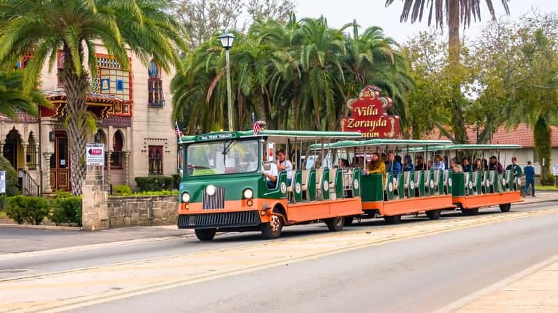Adult visitors riding a trolley past Villa Zorayda Museum, the former winter home of a Boston millionaire, during a tour of downtown highlights in this historic city. The trolley tour showcases notable landmarks and attractions in St. Augustine, Florida, catering to tourists and history enthusiasts.