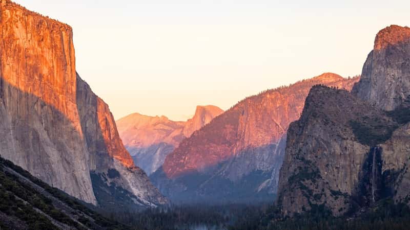 The image captures a stunning sunset scene in Yosemite National Park, California, showcasing the iconic Half Dome and El Capitan cliffs. 
