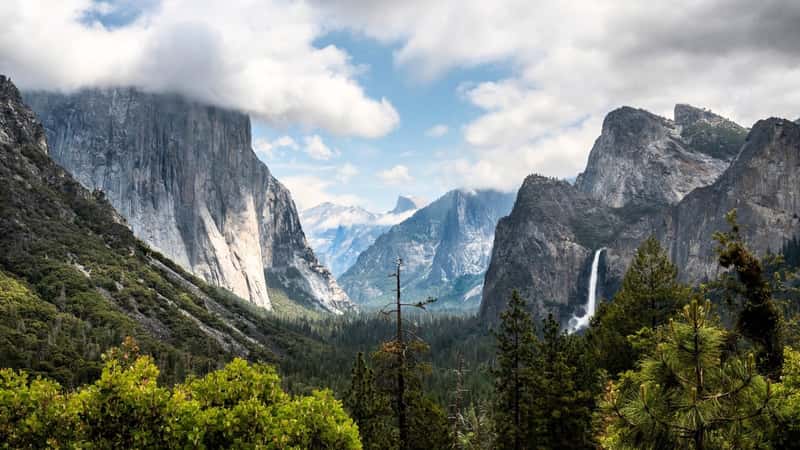 The image captures Yosemite National Park in California, showcasing the iconic Tunnel View with a majestic waterfall in the background. 