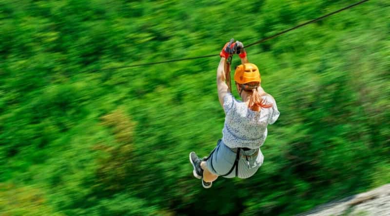A photograph illustrating the ziplining activity at Yunque Ziplining in Puerto Rico. The image captures individuals engaged in ziplining amidst the lush tropical landscape of the El Yunque National Forest.