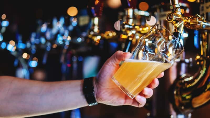 A photograph capturing a bartender's hand as they pour beer from a tap into a glass in a bar or pub setting. 