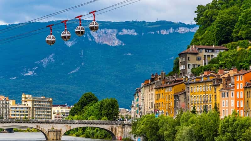Isere river in Grenoble city skyline, Auvergne-Rhone-Alpes region, France. Pont Marius-Gontard bridge, Grenoble-Bastille Cable car (Telepherique) and Alps mountains on background