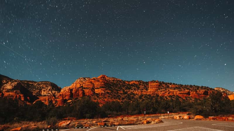 A photograph depicting the iconic red rock formations of Sedona illuminated against a nighttime sky. 