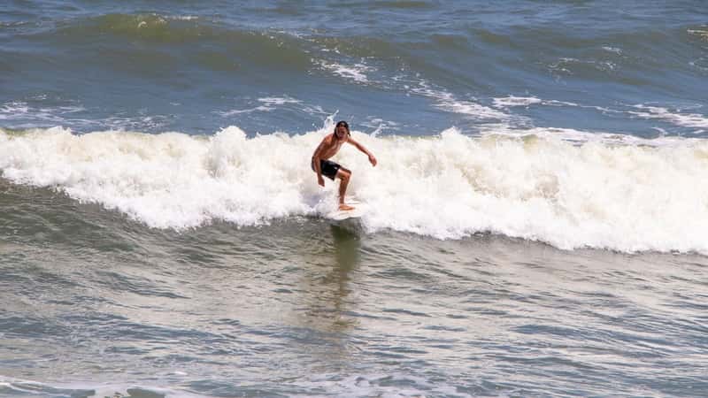 The image depicts a surfer on a board riding a wave in St. Augustine, Florida. The surfer is positioned in the center of the frame, with the wave curling behind them.