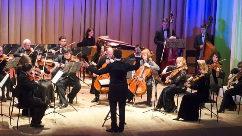 Tucson Symphony Orchestra in performance, featuring musicians on stage with various musical instruments and a conductor at the center.