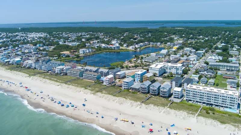 aerial shot of the coastline with green ocean water, waves, people on the beach, homes along the shore, Carolina Lake and lush green trees and grass in Carolina Beach North Carolina USA
