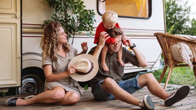Family trip, caravan camping lifestyle and recreation: young parents relaxing with small son at camper house having vacation in forest, picnic outdoors or road journey in mobile home or retro trailer