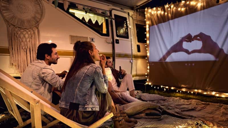 Group of young cheerful people watching a movie on camping site
