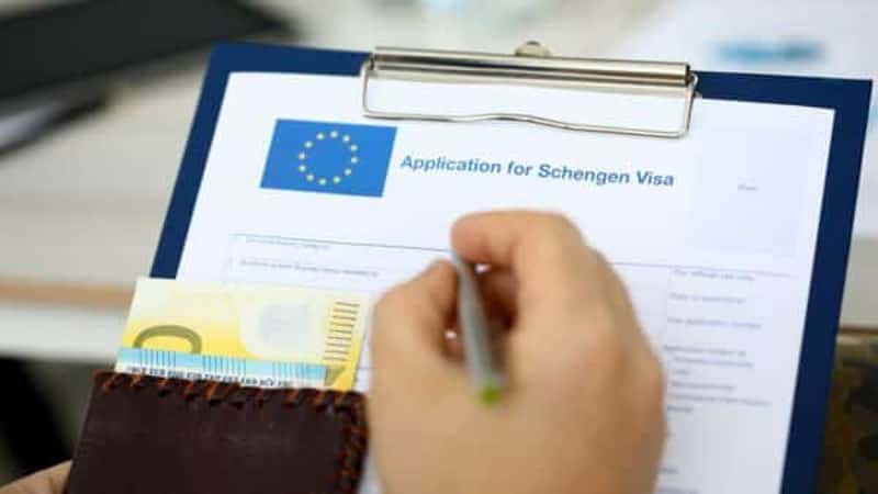 Male hand hold silver pen with passport. Filling Schengen apllication form concept
