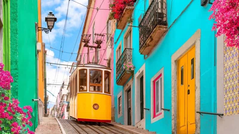 Lisbon, Portugal - Yellow tram on a street with colorful houses and flowers on the balconies - Bica Elevator going down the hill of Chiado