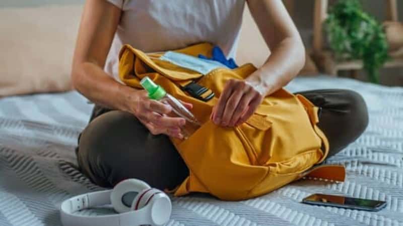 Close up of young woman packing her backpack with hand sanitizer.