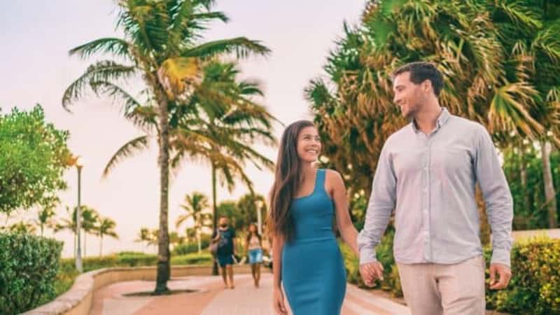 Miami people lifesyle happy couple walking on south beach enjoying city night out at sunset on summer travel vacation background.