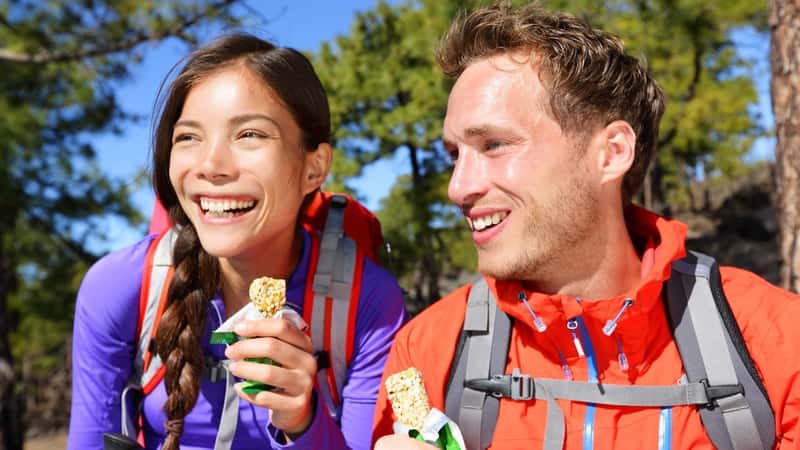 Happy people enjoying granola cereal bars living healthy active lifestyle in mountain nature.