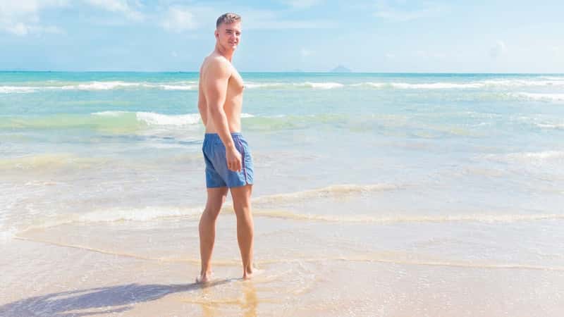 Handsome beautiful guy on the beach, young fit athletic slim guy man going to swim in the sea, walking on the sand, enjoying good sunny weather, sunbathing.