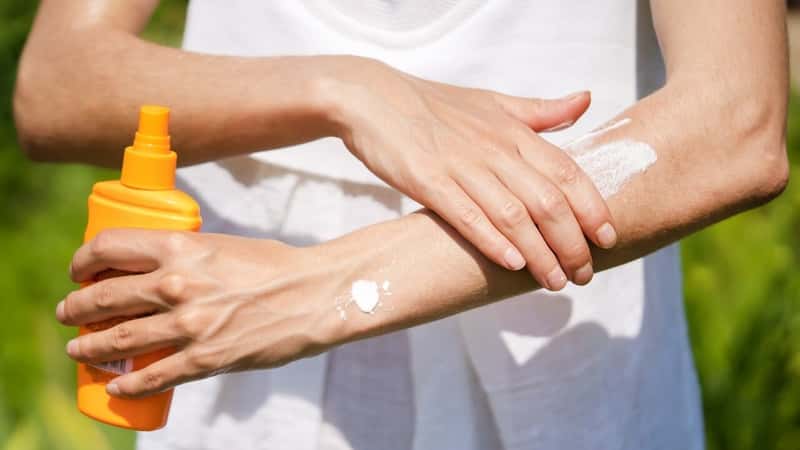 A young girl in a white summer dress applies sunscreen gel to her arms and shoulders, a woman takes care of her skin on a sunny day.