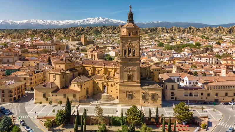Aerial view of Guadix old town, province of Granada, Andalusia, Spain. Historic Cathedral building, Alcazaba de Guadix fortress and snow capped Sierra Nevada mountain range at background