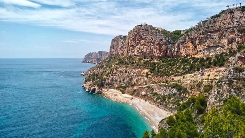 Aerial photo drone point of view picturesque Cala del Moraig in Benitachell coastal town. Bright turquoise waters bay of Mediterranean Sea white sandy beach, huge cliffs coastline. Costa Blanca. Spain