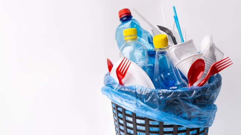 Say no to single use plastic. A black trash can with used plastic items isolated on white background, copy space