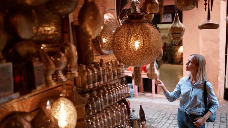 Travel and shopping. Young traveling woman with choose presents in copper souvenir handicraft shop in Morocco.