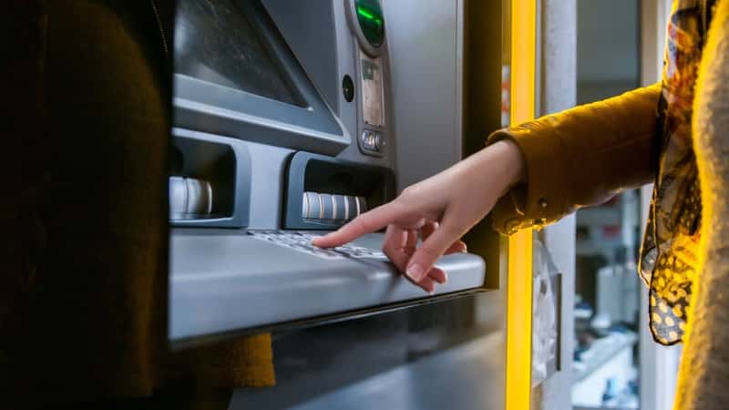 Lady using ATM machine to withdraw her money. Close-up of hand entering PIN/pass code on ATM/bank machine keypad. Finger about to press a pin code on a pad. Security code on Automated Teller Machine.