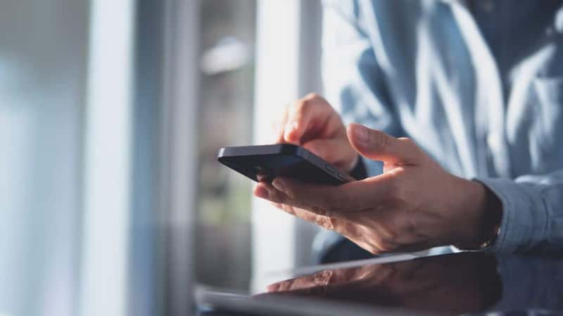 Close up, business woman using mobile smart phone on glass table with reflection and sunlight. Woman using smartphone during working at office with digital tablet on table, social network