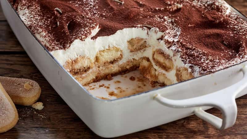 Dish of homemade tiramisu Italian desert with ladyfinger biscuits, coffee and marscapone cheese in a panorama banner on a rustic table