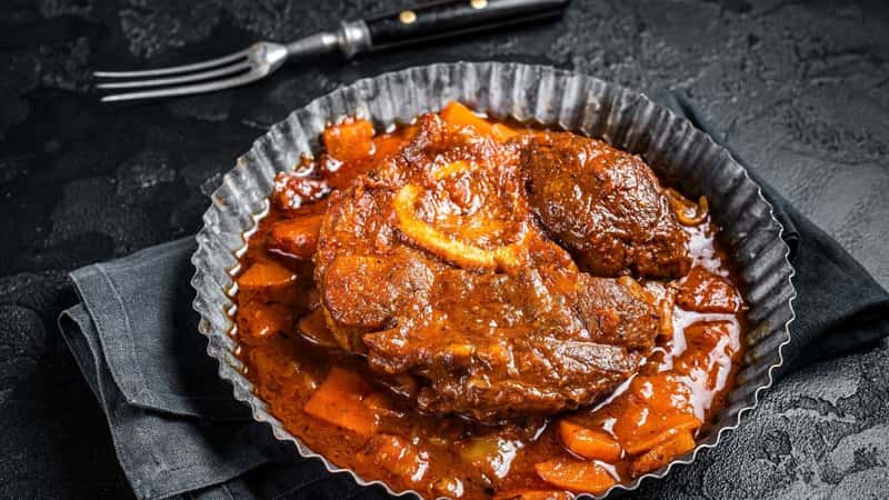 Braised meat on the bone Osso Buco in tomato sauce, veal italian meat Ossobuco. Black background. Top view.