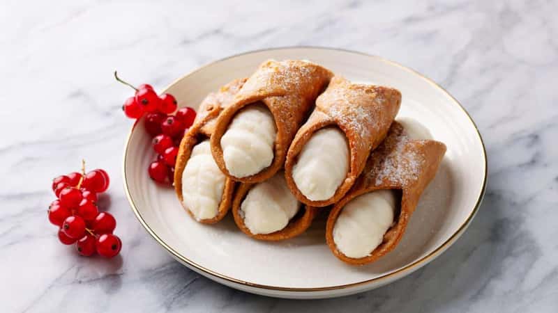 Cannoli Italian dessert on a plate with red currant berries. Marble background. Close up.