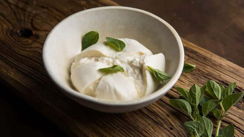 Whole tied Italian cheese burrata on small wooden cutting board served with fresh oregano