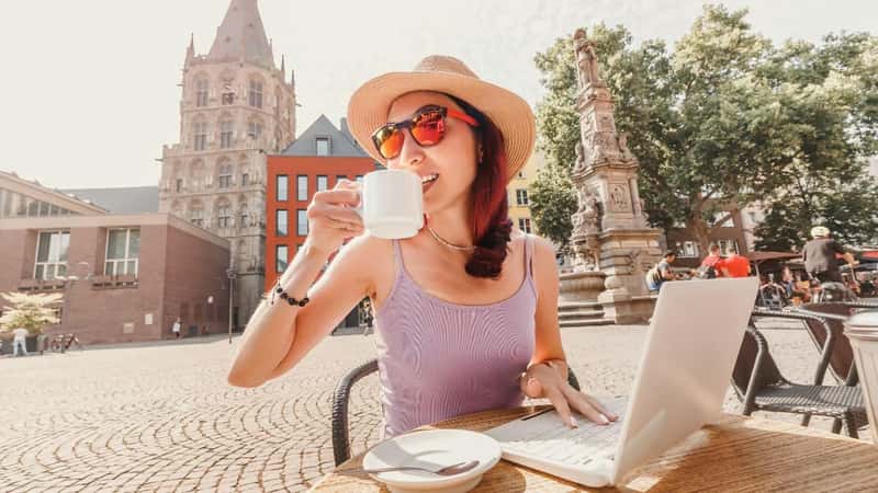 A girl drinks coffee in an old European city of Cologne and works or studies on a laptop. Remote employment and student life