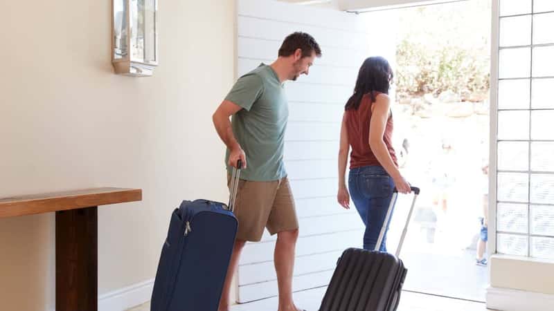 Mid adult white couple at their front door leaving home with luggage to go on vacation, full length