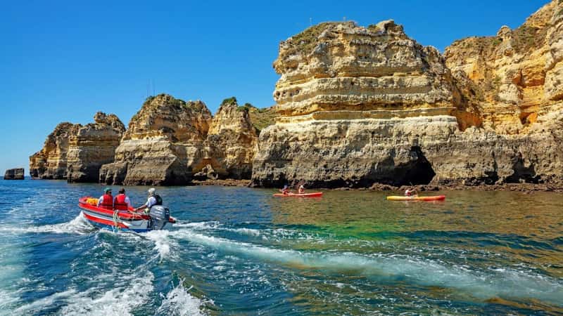 Ponta da Piedade, The Algarve, Portugal, June 16th, 2021, a small boat with tourists on a guided tour and kayakers about to enter the caves and grotto.