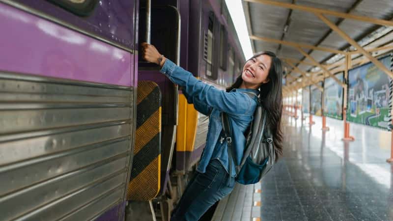 Happy asian tourist getting on the train at the station, beginning her journey