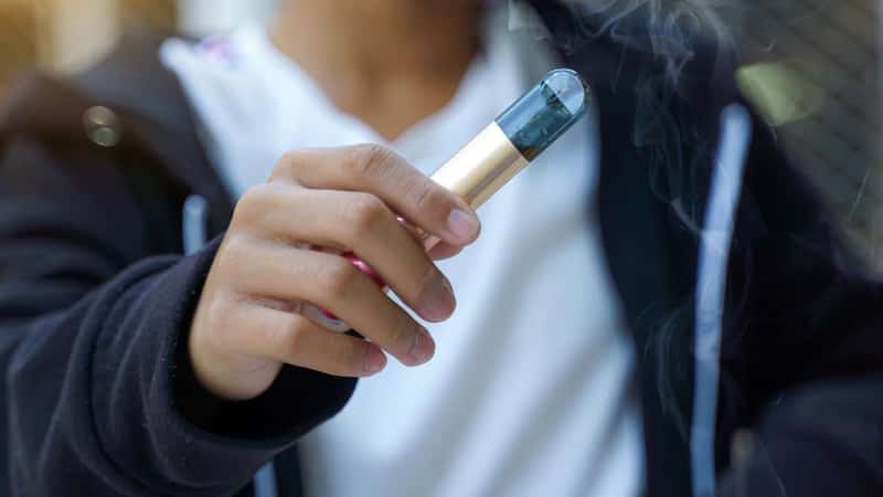 Close-up of a young Asian male hand holding an electronic cigarette. Concept of teenagers, substance abuse, behavior, cigarettes, harms of cigarettes.