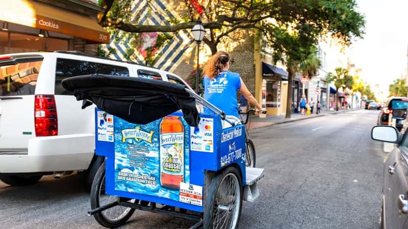 Charleston, USA - May 12, 2018: Woman riding guided tour rickshaw at French quarter old town on King street in South Carolina with cars in traffic at sunset