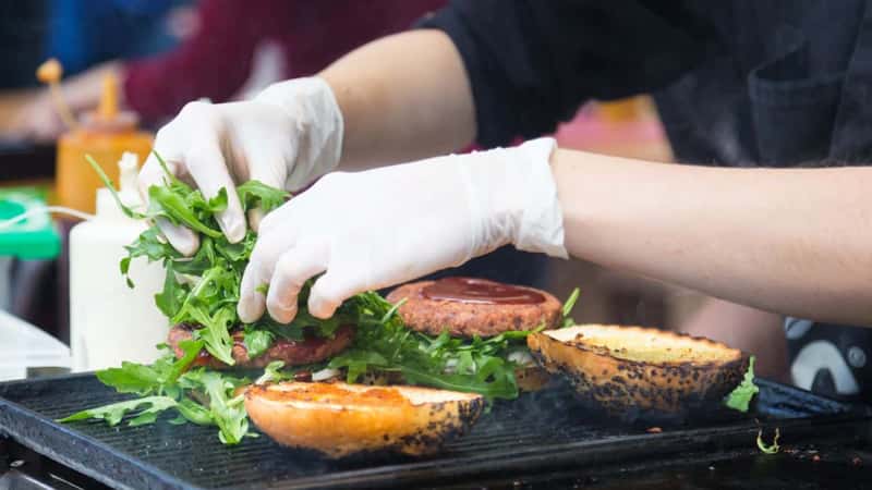 Chef making beef burgers outdoor on open kitchen international food festival event. Street food ready to serve on a food stall.