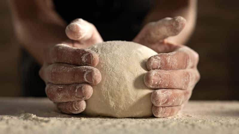 Cinematic close up of professional artisan baker chef is making with flour loaf of dough for preparation of pasta, pizza and other pastries in rustic bakery kitchen.