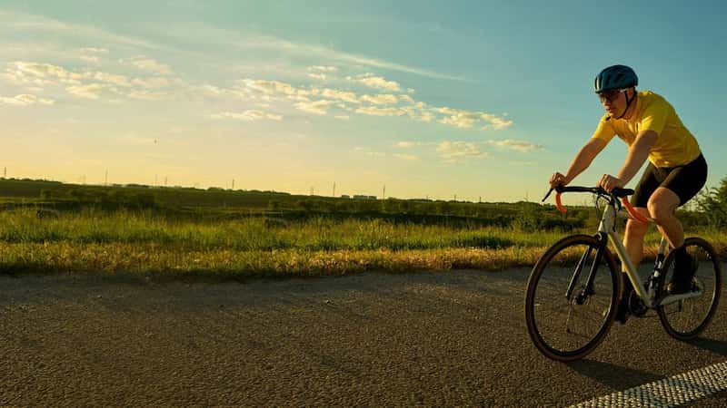 Cyclist on open road wearing yellow top and black shorts, enjoying long solo ride through countryside with motion blur effect. Banner. Concept of freedom, adventure, sport training, nature.