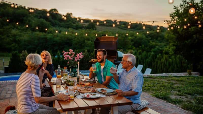 Happy family eating together outdoors. Smiling generation family sitting at dining table during dinner. Happy cheerful family enjoying meal together in garden.