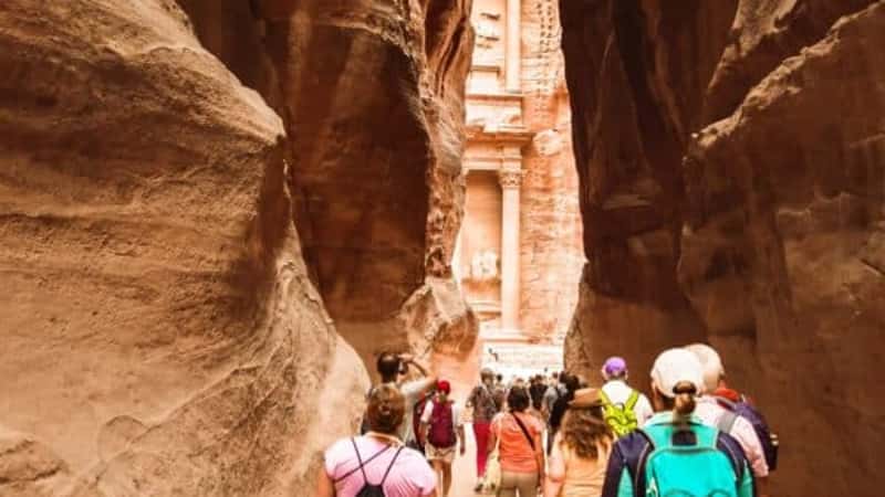 Tourists walk towards treasury landmark in Petra through The Siq, the narrow slot-canyon that serves as the entrance passage to the hidden city of Petra, Jordan